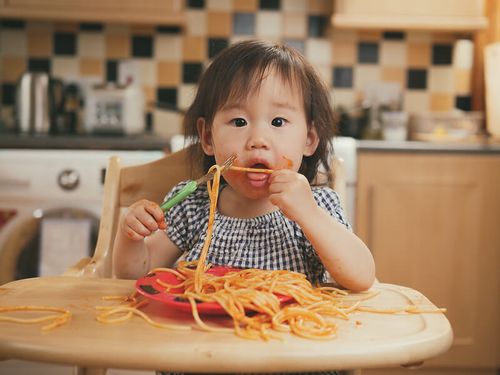 Toddler enjoying their pasta in a high chair.