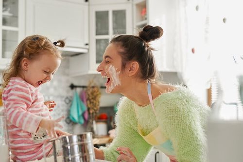Mother and daughter getting messy in the kitchen making a cake.