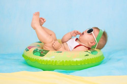 Baby wearing sunglasses with its legs in the air whilst lying in an inflatable ring on holiday.