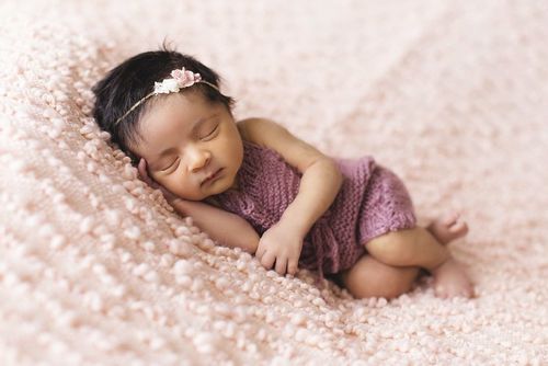 Baby girl wearing a flower hairband sleeping on a pink blanket. 
