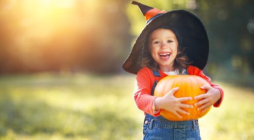 Young girl dressed for Halloween holding a pumpkin smiling.