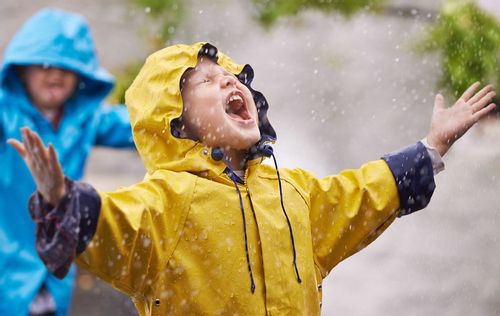 Kids wearing raincoats messing around and getting wet in the rain.