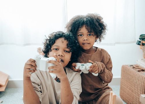 Two kids holding white games console controllers playing video games.