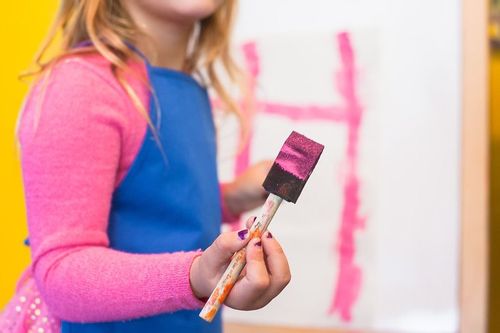 Girl holding a sponge brush with pink paint on it ready to do some Viking arts and crafts.