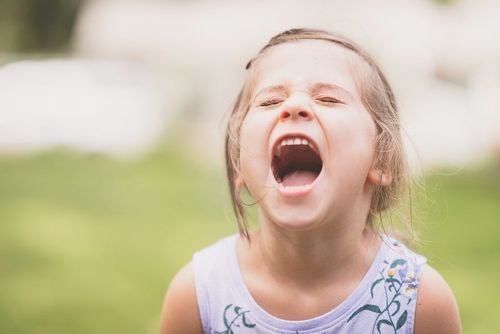 Little girl in the garden laughing with her mouth wide open at bear jokes.