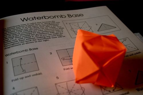 An origami water bomb resting on the page of an open book containing a guide for making an origami water bomb.