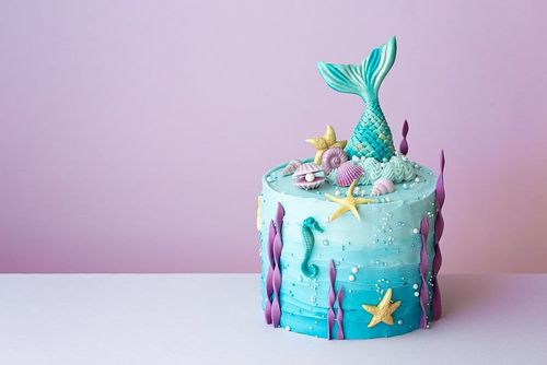 Magical mermaid cake, with sea icing decorations and a mermaid tail sticking out the top.