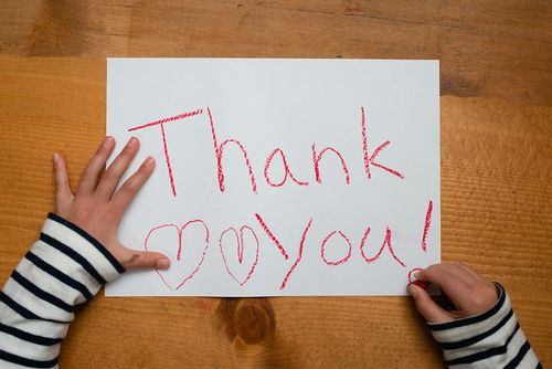 Child has written 'thank you' in red crayon on a piece of paper.