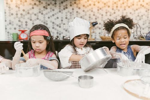 Three young girls in the kitchen baking a cake.