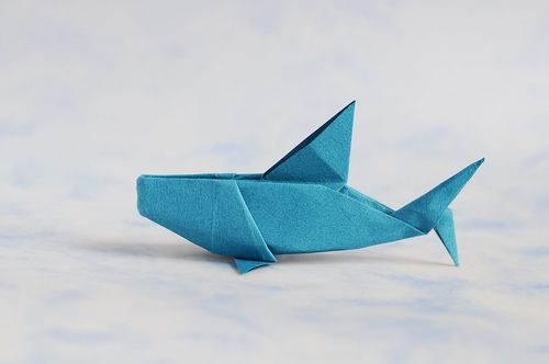 A blue origami shark on a light blue and white marbled surface.