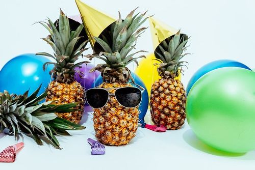 Funny pineapple party: pineapples wearing sunglasses and party hats with balloons around them.