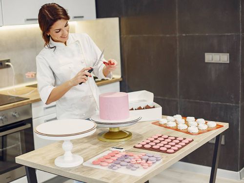 Pastry chef in the kitchen decorating an elaborate pink cake.