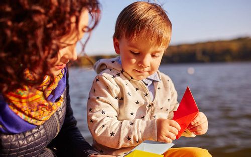 Mum and son sat together on a boat making an origami dolphin.