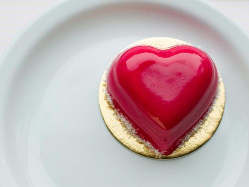 Small, individual-sized red, heart shaped cake on a plate.