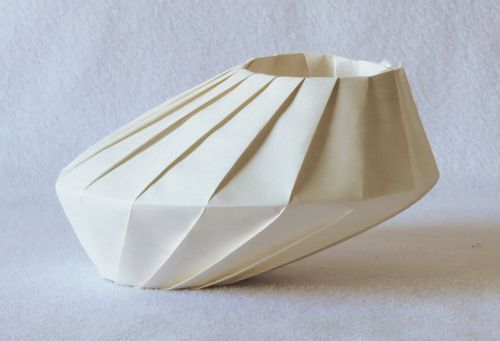 A white origami bowl placed on a white surface.