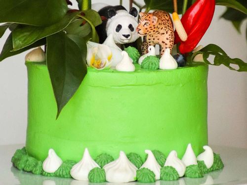Bright green cake with jungle animal figures, including a panda and a tiger, on top.