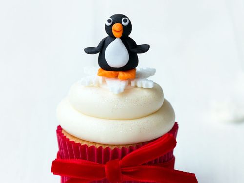 A cupcake in a red case with white frosting and an icing penguin figure on top.