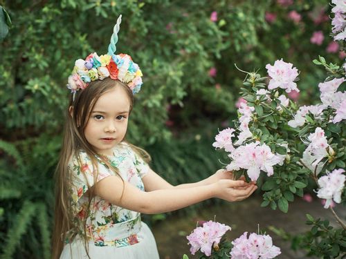Little girl wearing a DIY unicorn horn as she reaches for some flowers in the garden.