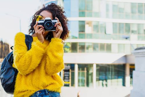 Teenage girl in a yellow jumping holding a camera up to her face taking a photo.