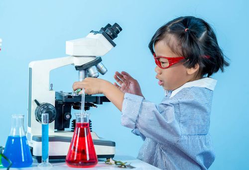 Young girl sat looking at a microscope doing a science experiment.