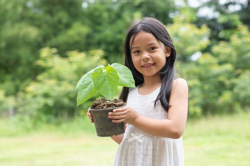 Young girl standing in a garden holding a plant in her hands smiling.