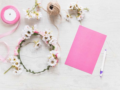 A flower wreath, some string, a pen and a piece of pink paper on a table.
