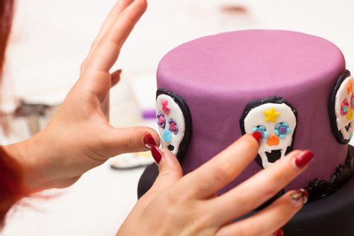 Close up of woman's hands as she sticks skull icing decorations on the side of a purple pirate birthday cake.