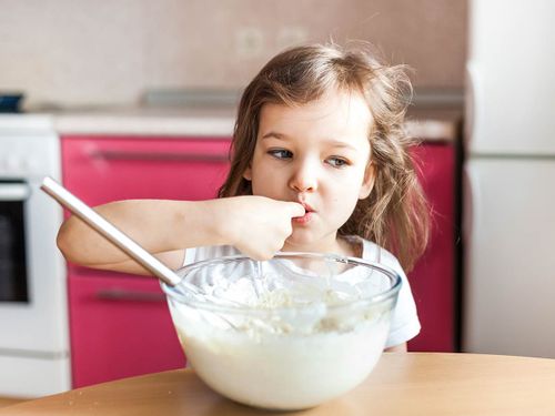 Little girl sneaks a taste of the ladybird cake mixture from the bowl.