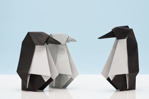 Three completed origami penguins, two are black and white and one is grey and white, standing against a blue background.