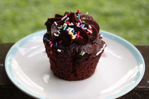 A close up image of a giant chocolate cupcake with rainbow coloured sprinkles on top.