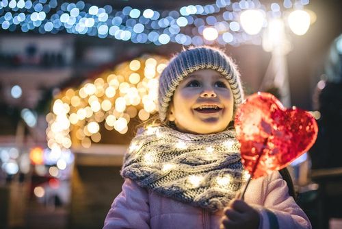 Little girl wrapped up in a scarf and hand smiling and enjoying the lights and festivities at Christmas time.