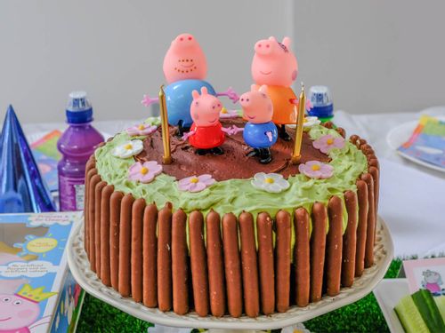 Peppa Pig birthday cake with chocolate fingers around the edge and figurines on top.