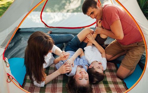 Family lying in a tent laughing on their camping holiday in the UK.