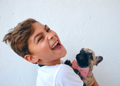 A boy looks at the camera and laughs out loud at a New Year joke whilst holding a puppy.