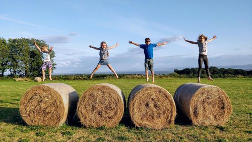 Four children jumping on hay bales at a farm.