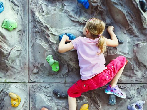 Little girl wearing pink climbing up a rock wall.