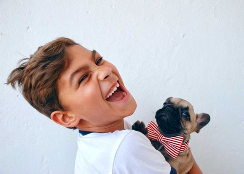 Young boy smiling while holding a pug wearing a bow.