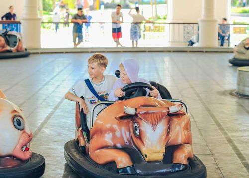 Two boys sat driving in a bumper car smiling and having fun.