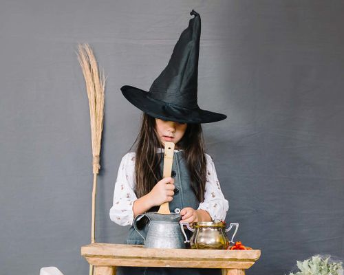 A little girl dressed as a magical witch is casting spells.