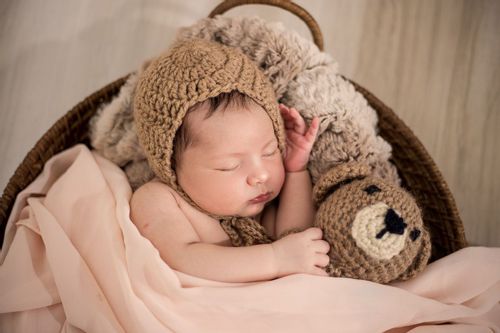 A newborn baby wearing brown knitted cap sleeping with teddy
