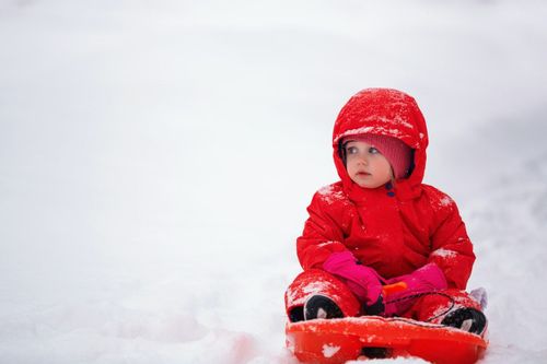 A baby wearing red winter clothes in snow
