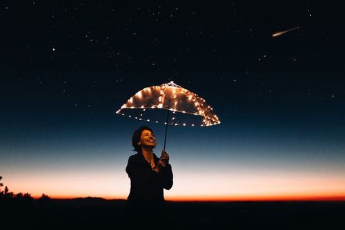 A woman holding an umbrella with fairy lights under the night sky