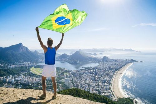 A man holding Brazilian flag over the cliff