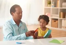 Vater und kleine Tochter saßen am Tisch mit Papier, um ein Wikinger-Langbootmodell herzustellen.