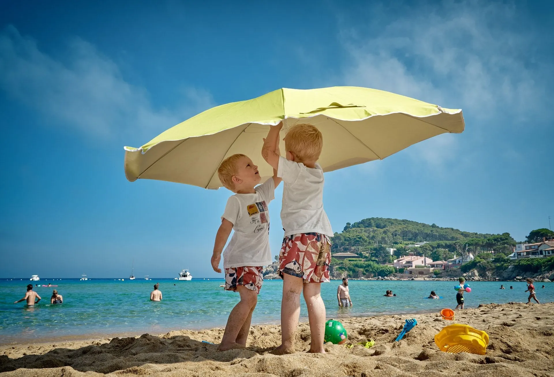 Two little boys setting up an umbrella on beach