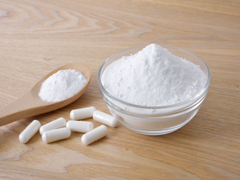 White Taurine powder and capsule on wooden table.